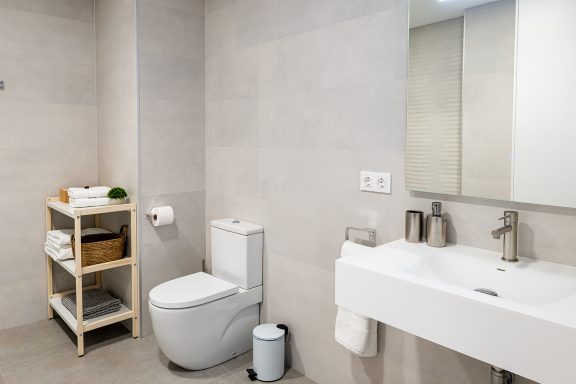 Baño moderno con inodoro, lavabo y estantería con toallas y artículos de higiene.