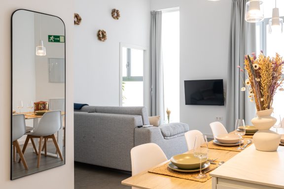 Interior de un salón moderno con espejo, mesa, sillas, sofá y decoración minimalista.