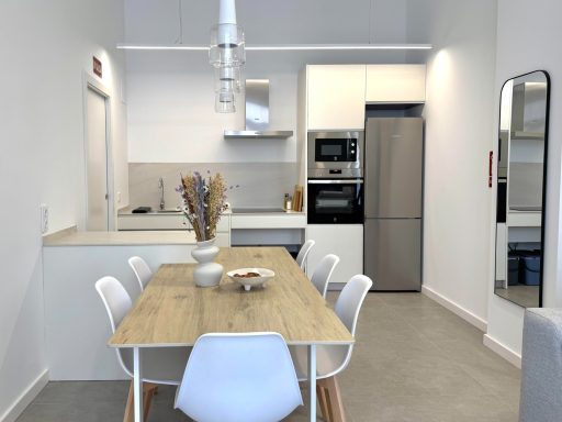 Cocina moderna con mesa de comedor, sillas blancas y electrodomésticos de acero inoxidable.